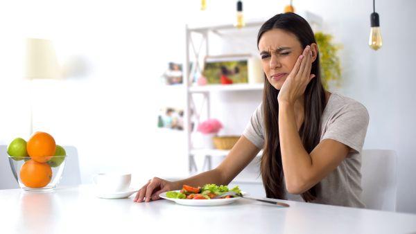 Woman holding jaw in pain while eating a meal